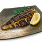 Grilled fish fillet on a ceramic plate with a lemon wedge and green garnish.