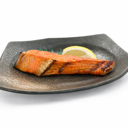 Grilled salmon on a black plate with a lemon wedge on a white background